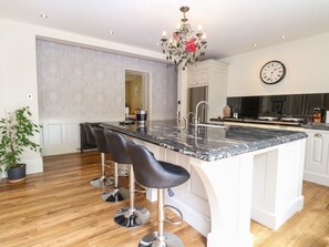 A kitchen with a marble countertop, bar stools, a chandelier, and a clock on the wall. - The Farmhouse in North Walsham (North Walsham)