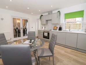A modern kitchen with grey cabinets, a round glass table, and a dining area with grey chairs. - 4 Manor Garth near Withernsea. (Withernsea)