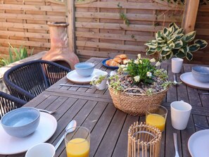 A wooden table with breakfast items, a woven basket with flowers, and a rustic vase. - Charming Beehive Cottage in Beccles (Beccles)