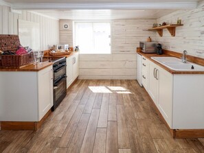 A kitchen with wooden flooring, white cabinets, a microwave, and a sink. - Charming Beehive Cottage in Beccles (Beccles)
