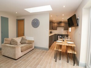A modern kitchen with a flat-screen TV, a dining table with chairs, a sofa, and a wall clock. - Charming Premium Cottage 7 (Durham)
