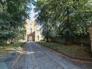 A stone pathway leading to a historic building with an arched entrance and a clock tower. - Charming Premium Cottage 7 (Durham)