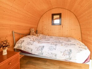 A cozy room with a wooden interior, a bed with floral bedding, a teddy bear, and a small window.