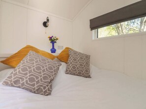 Ein Schlafzimmer mit Bett, Kissen, einer Vase mit Blumen, einer Wandleuchte und einem Fenster.