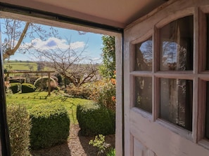 A doorway leading to a garden with a wooden bench, neatly trimmed hedges, and a clear view of the countryside. - Magnolia View, Barnstaple (Barnstaple)