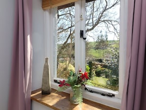 A window with a view of a garden, a vase with flowers, and a decorative bottle. - Magnolia View, Barnstaple (Barnstaple)