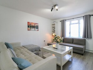 A living room with a sofa, a coffee table, a painting, a cabinet, and a window with curtains. - The Alex: Modern Living in Deptford (Deptford)