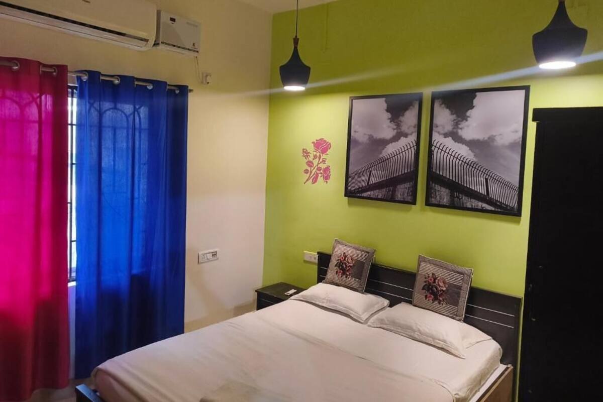 A bedroom with a bed, two nightstands, a wall-mounted air conditioner, and two wall-mounted pendant lights.