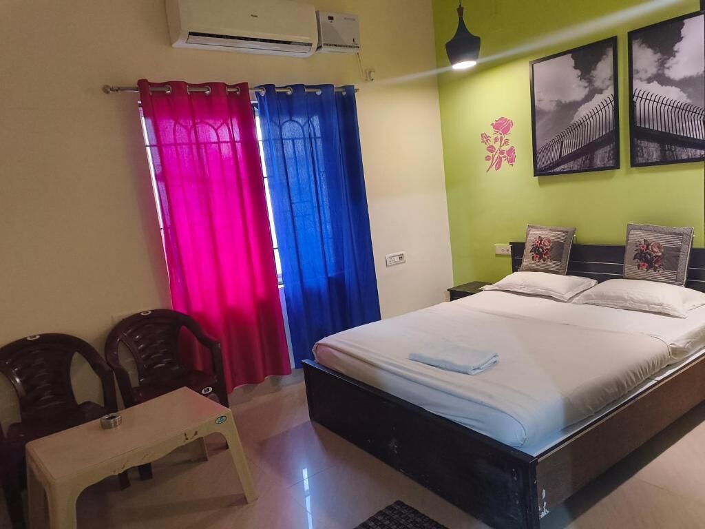 A bedroom with a bed, a desk, chairs, and a wall-mounted air conditioner.