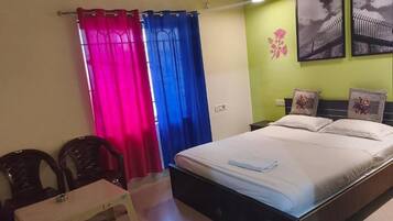 A bedroom with a bed, a desk, chairs, and a wall-mounted air conditioner.