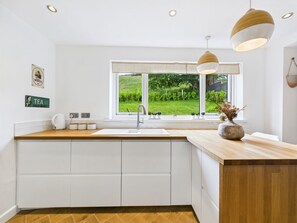A modern kitchen with a large window, white cabinetry, and a wooden countertop.