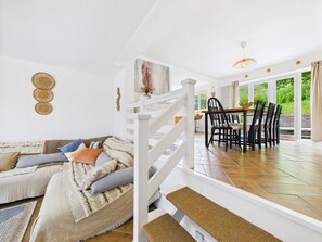 A modern interior with a white staircase, a dining area with black chairs, and a view of greenery outside.