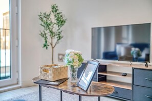 Ein modernes Wohnzimmer mit Fernseher, einem kleinen Tisch mit Blumen und einem Korbbasket sowie einem gerahmten Bild.