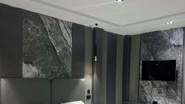 Een moderne slaapkamer met een groot bed, een flatscreen televisie aan de wand en een wand met een marmerpatroon.