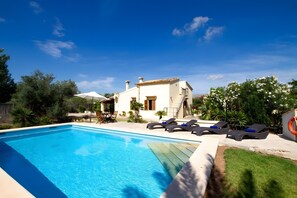A swimming pool with lounge chairs, a white building, and surrounding greenery. - Villa 'L'Embat' with Mountain View, Private Pool and Wi-Fi (Illes Balears)