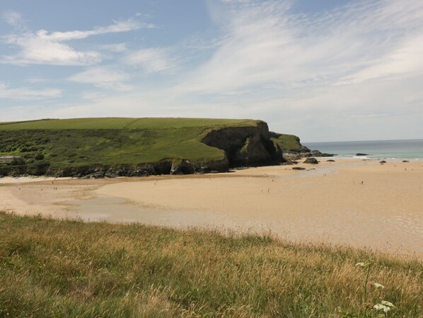 A coastal landscape with a sandy beach, grassy hills, and a prominent rock formation. - Woodlands Close, Padstow (Padstow)