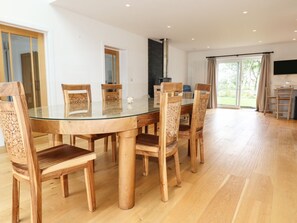 A dining area with a glass-top table surrounded by wooden chairs, a chimney, and a view of the outdoors. - Woodlands Close, Padstow (Padstow)