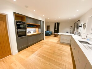 A modern kitchen with built-in appliances, a dining area with a table and chairs, and a cozy seating area with a sofa. - Woodlands Close, Padstow (Padstow)