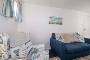 A living room with a sofa, a blue armchair, and a painting on the wall. - Seaside Apartment, Looe (Looe)