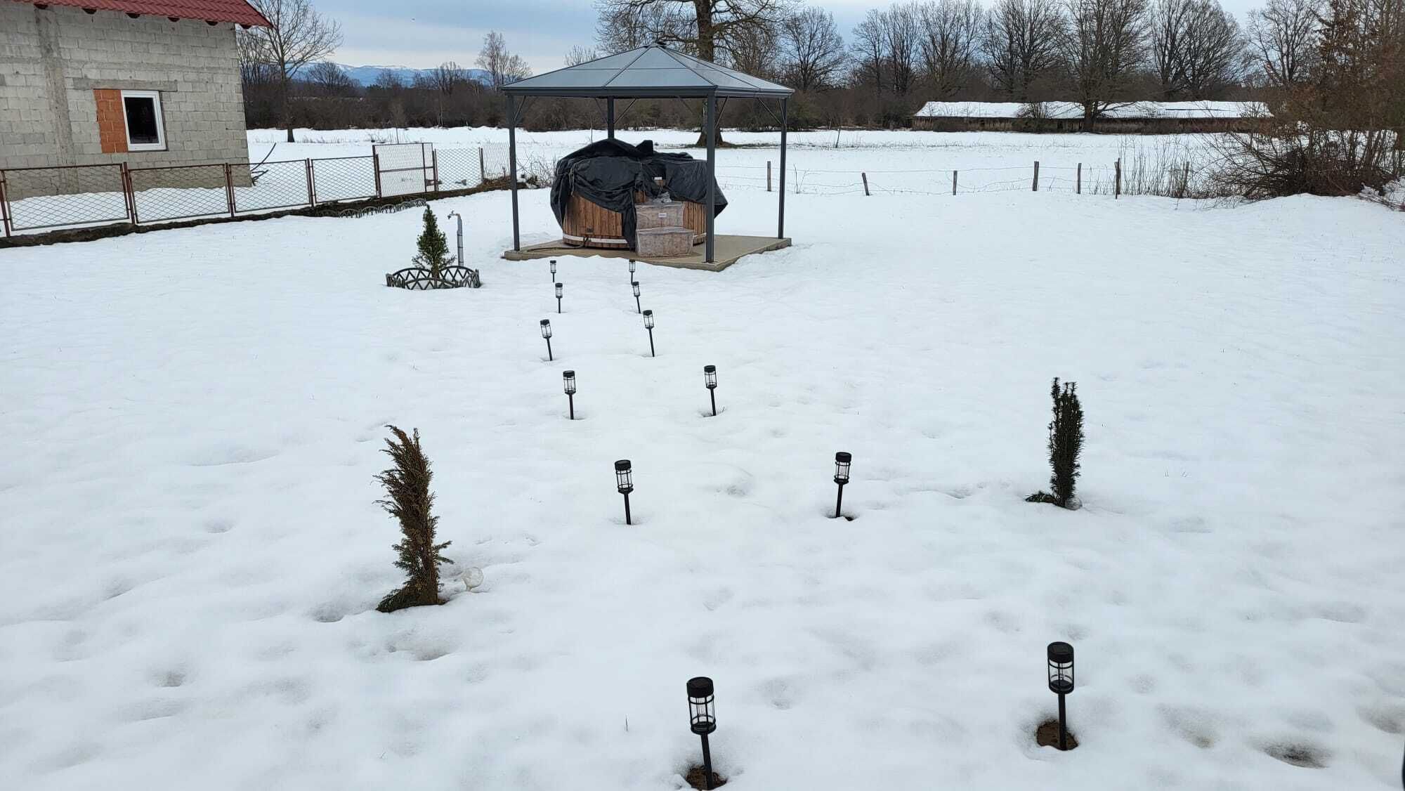 A snow-covered outdoor area with a gazebo, a fenced building, and a small tree.