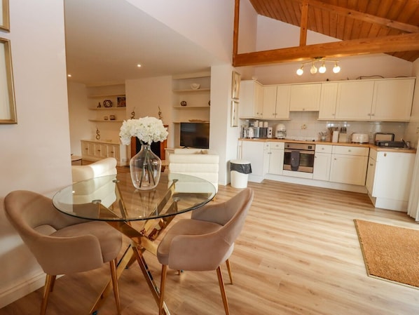 A modern kitchen with white cabinets, a dining area with a glass table and two chairs, and a wooden floor. - Snowdrop, Blandford Forum (Blandford Forum)