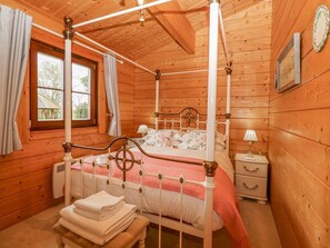En seng med himmelseng, et natbord med lampe, et vindue med gardiner og en trævæg med billedramme.