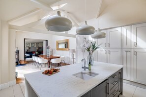 A modern kitchen with white cabinetry, a large island with a sink, pendant lighting, and a dining area with a wooden table and chairs. - The Old Chase, Chester (Chester)