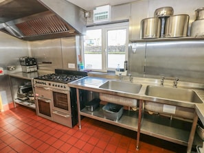 A commercial kitchen with stainless steel appliances, a large sink, and a window providing a view outside.