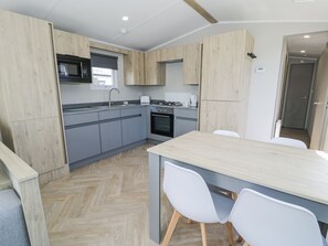 Una cocina moderna con armarios grises, encimera de madera y comedor con sillas blancas.