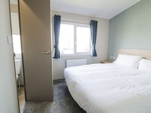 Una habitación de hotel con una cama, un ventanal con cortinas, un radiador y una puerta que da a un baño.