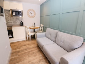 A compact living space with a kitchenette, a sofa, a dining table, and a clock on the wall.