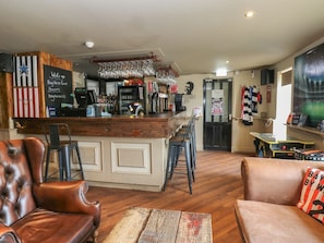 A bar area with a wooden counter, stools, and a barista station. There are leather chairs and a table with a patterned table runner.