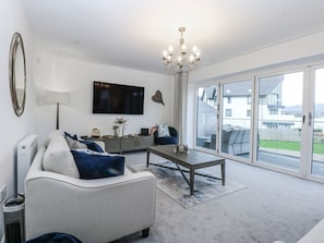 A modern living room with a sofa, coffee table, and a TV mounted on the wall. - Estuary View, Llansanffraid Glan Conwy (Colwyn Bay)