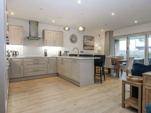 A modern kitchen with a central island, wooden flooring, and a dining area with a table and chairs. - Estuary View, Llansanffraid Glan Conwy (Colwyn Bay)