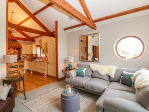 Ein gemütliches Wohnzimmer mit einem grauen Sofa, einem runden Spiegel und einem Fenster.
