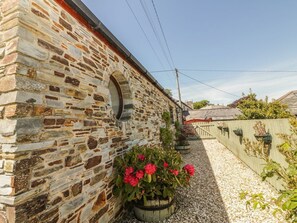 Ein Gebäude aus Stein mit Kiesweg, Pflanzgefässen und blauem Himmel.