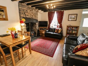 Ein gemütliches Wohnzimmer mit Kamin aus Stein, einer schwarzen Ledersofa, einem Holzesstisch und einem roten Teppich mit Muster.