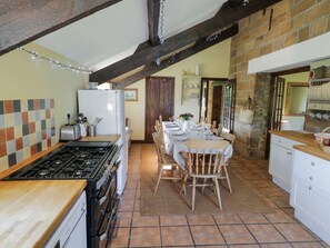 A kitchen with a gas stove, wooden chairs, a dining table set for four, and a stone wall. - Dale View, Lealholm, Whitby (Whitby)