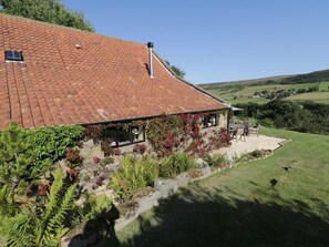A house with a tiled roof, a covered porch, and a garden with various plants. - Dale View, Lealholm, Whitby (Whitby)