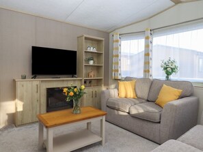 Una sala de estar con televisor, estanterías de madera, un sofá con cojines amarillos y una ventana con cortinas.