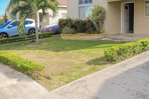 A residential area with a well-maintained lawn, a covered car, and a building with a door and windows. - Caymanan Estate Near Ocho Rios (Spanish Town)