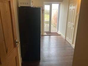 Ein Flur mit einem Kühlschrank, einer Tür zu einer Terrasse und einer Fußmatte am Eingang.