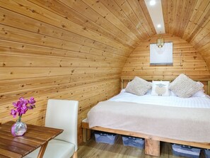 A cozy wooden room with a bed, a small table with a vase of flowers, and a window with blinds. - The Pod at Bank House Farm, Hixon (Stafford)