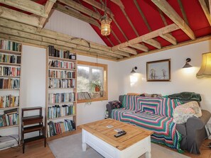 Ein gemütliches Zimmer mit Bücherregal, einer Couch mit bunter Decke, einem Holztisch und einer roten Decke an der Decke.