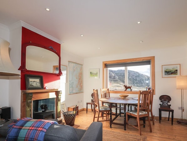 Ein Essbereich mit Holztisch und -stühlen, einem Kamin und einem großen Fenster mit Blick auf die Berge.