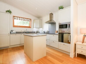 Moderni keittiö, jossa on valkoiset kaapit, keskellä oleva keittiösaareke, mikroaaltouuni ja uuni.