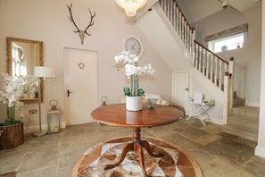 A foyer with a round wooden table, a mirror, a clock, a staircase, and a decorative antler on the wall. - The Coach House, Bolney Sussex (Haywards Heath)