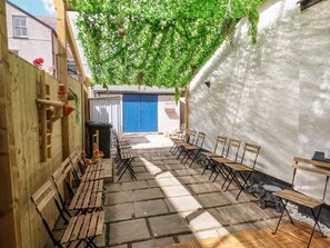 An outdoor seating area with wooden benches and a stone floor, surrounded by a wooden fence and a white wall. - The Bookcase, Colwyn Bay (Colwyn Bay)