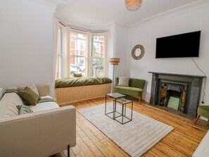 A living room with a sofa, a green armchair, a fireplace, and a television. - The Bookcase, Colwyn Bay (Colwyn Bay)