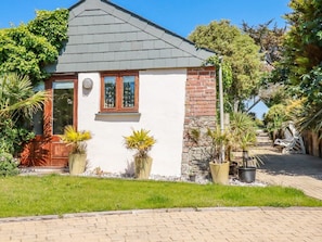 A house with a white exterior, a brick section, a grey roof, and a front door with a window. There are potted plants and a pathway leading to the entrance. - Cameo, Bude, Cornwall (Bude)